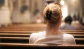 This photograph is taken from the back pew and shows the back of a woman's head, a woman who is also sitting in the back.  In the foreground is the blurred scene of a service in progress.